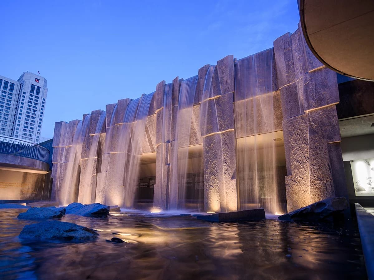 Water pouring over the granite walls of the Martin Luther King Jr. Memorial in Yerba Buena Gardens at twilight, lit from below, with glass panels behind the falls