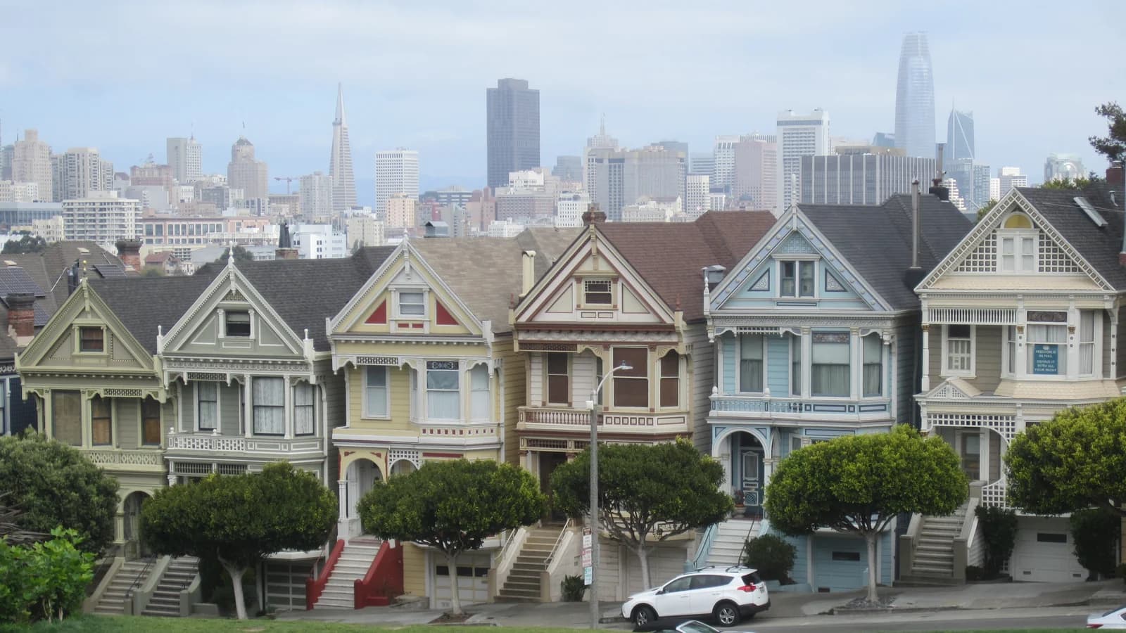 The row of pastel Victorian Painted Ladies houses on Steiner Street with the downtown skyline behind and Alamo Square's lawn in front
