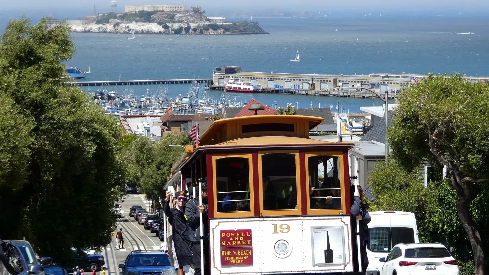 A Powell-Hyde cable car climbing Hyde Street on Russian Hill with riders on the running boards, Alcatraz and the bay beyond