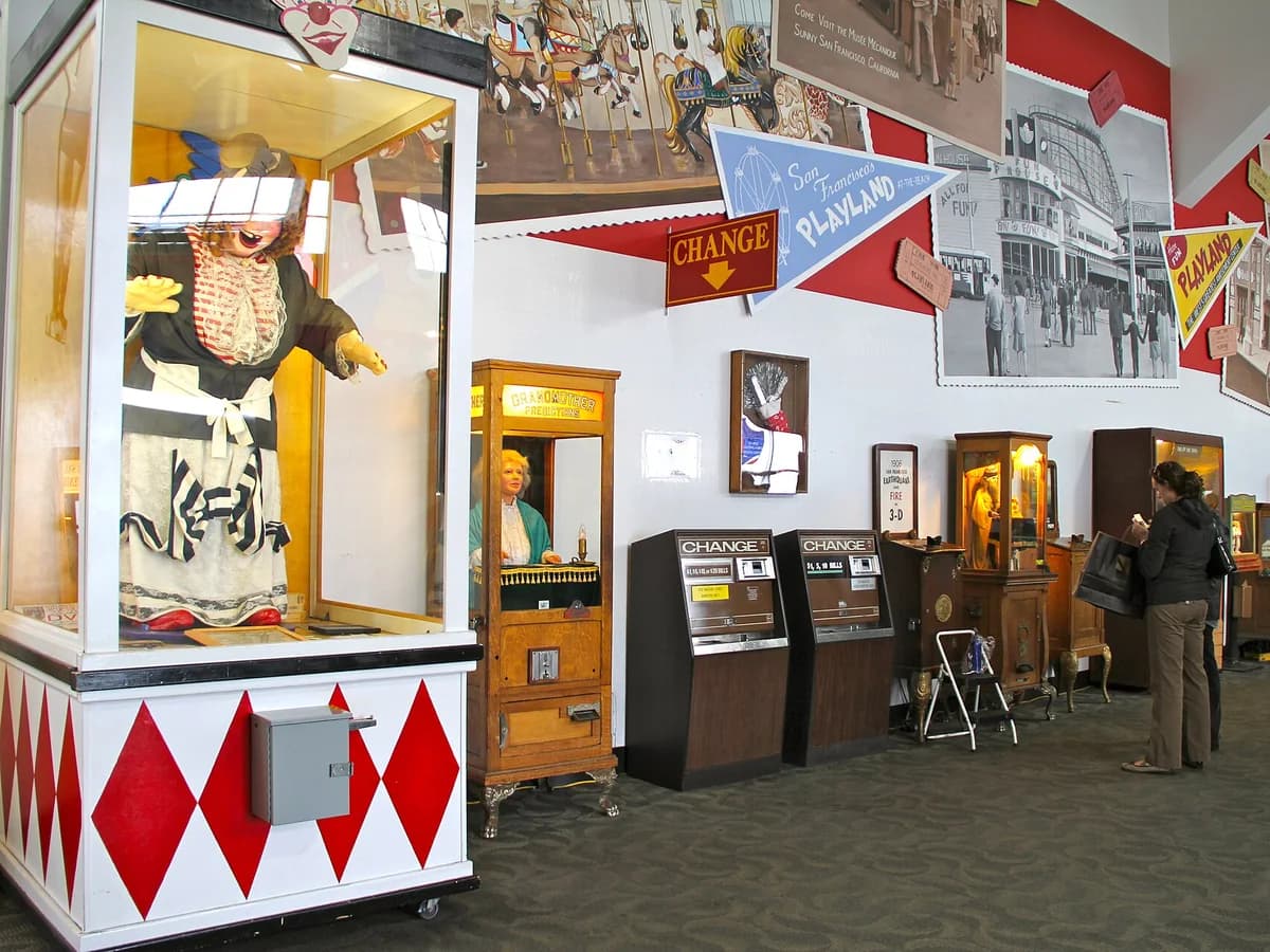 Laffing Sal in her glass booth with red diamond panels, beside a row of antique fortune-teller and coin-op cabinets and change machines along a Playland-themed wall