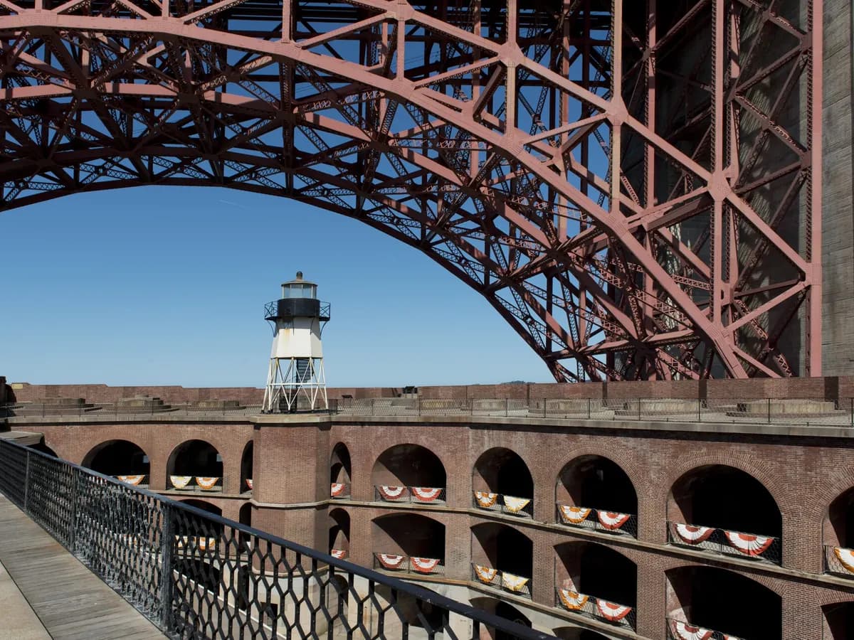 The brick casemate tiers of Fort Point's courtyard and its small rooftop lighthouse, framed by the huge steel arch of the Golden Gate Bridge overhead
