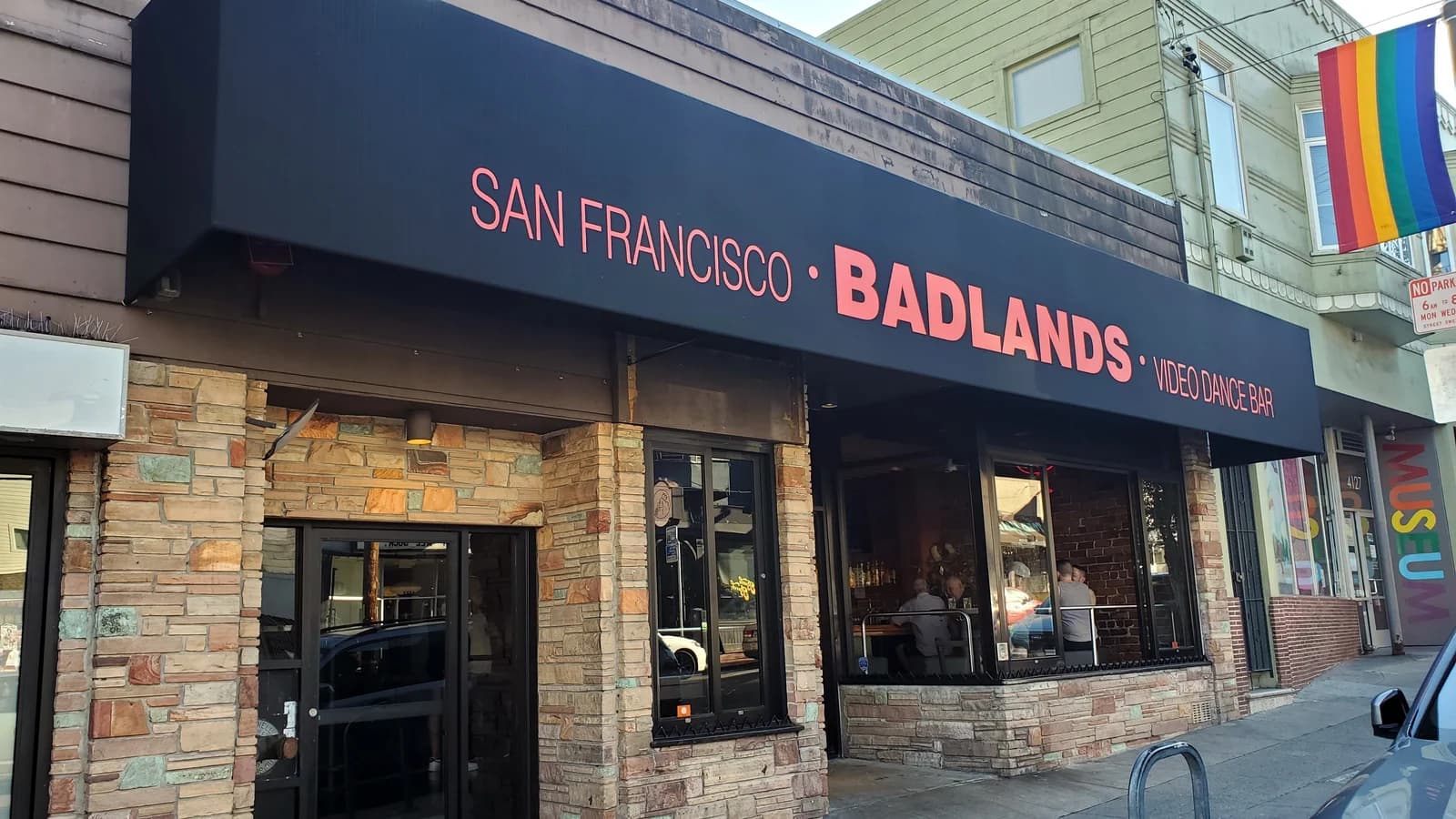 The black Badlands Video Dance Bar awning over a stone-clad storefront on a sunny day, with a rainbow flag hanging from the building next door