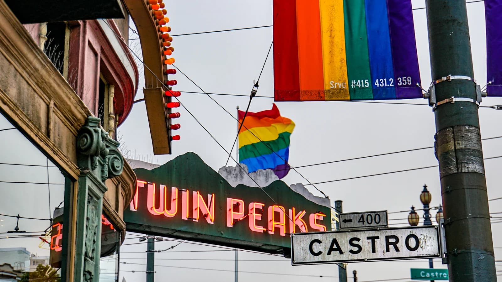 Neon Twin Peaks Tavern sign under rainbow flags beside the Castro street sign in San Francisco