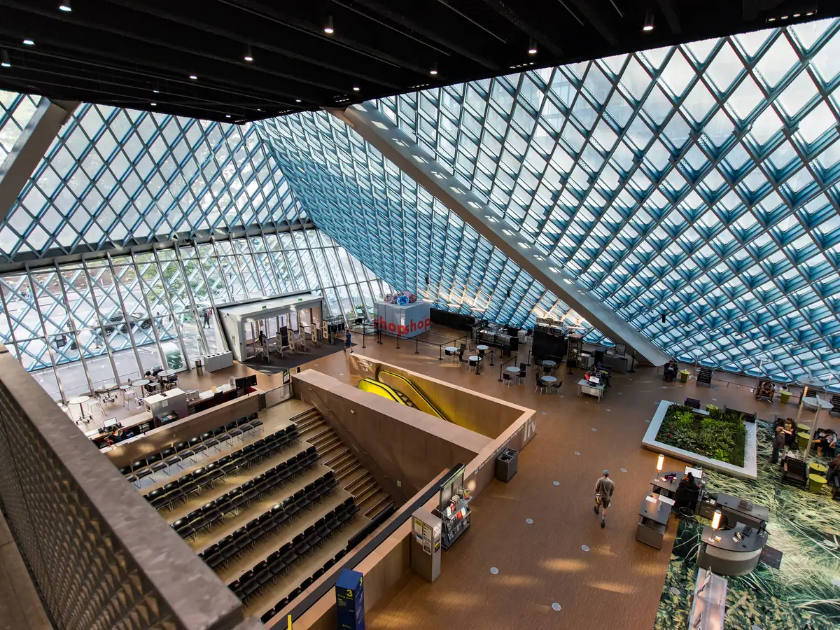 Inside the Seattle Central Library, a slanted glass and steel diamond grid ceiling rises over reading areas and a wide sloping staircase