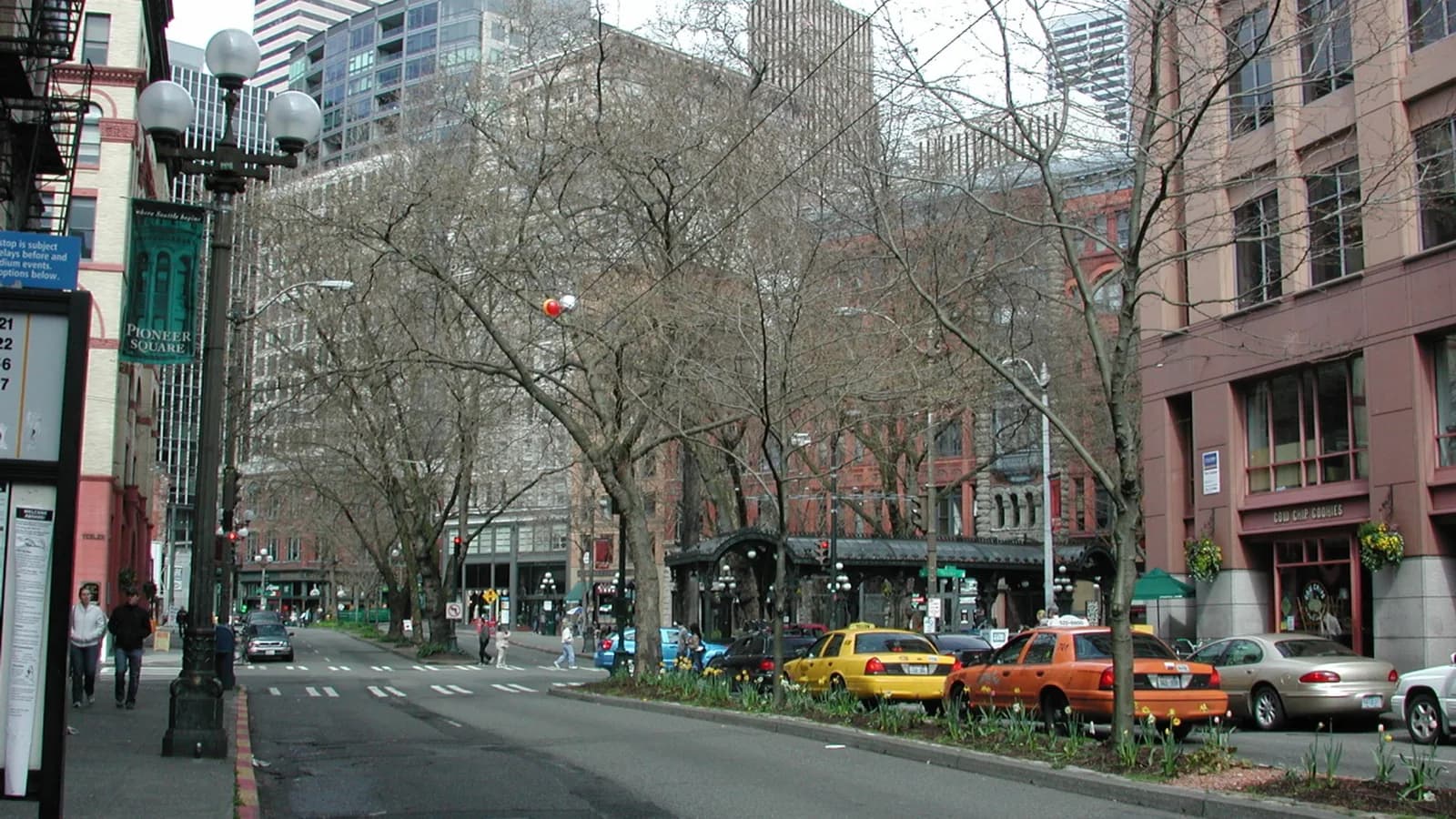 Brick and stone buildings along a Pioneer Square street in Seattle, with old lamp posts, bare trees and the iron pergola in the distance