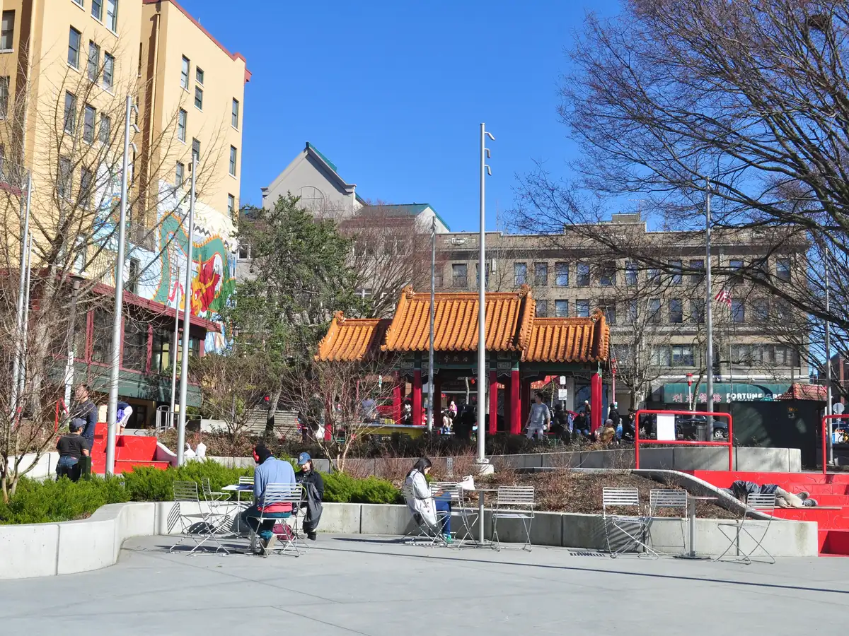 Hing Hay Park in Seattle's Chinatown, with an ornate red and gold pavilion, a paved plaza with benches and people sitting in the sun