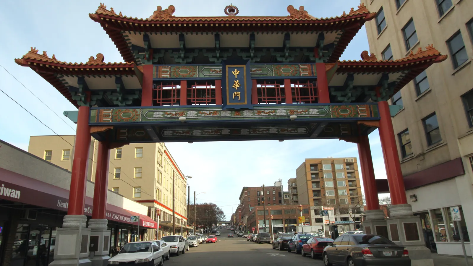 The ornate Chinatown gate over South King Street in Seattle, with red columns and a tiled roof, and shops along the street behind it