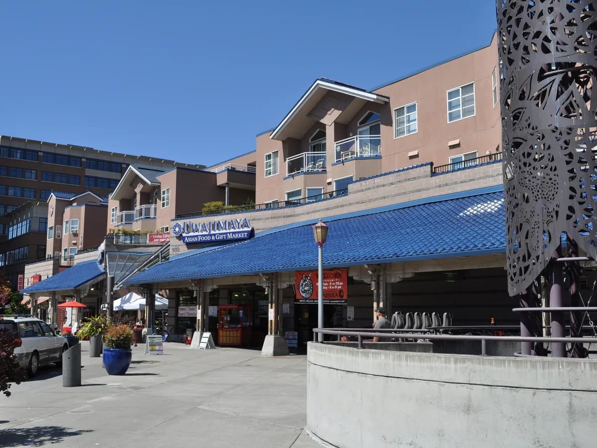 The Uwajimaya store building in Seattle, with blue awnings over the entrance, a large decorative metal panel and people on the sidewalk