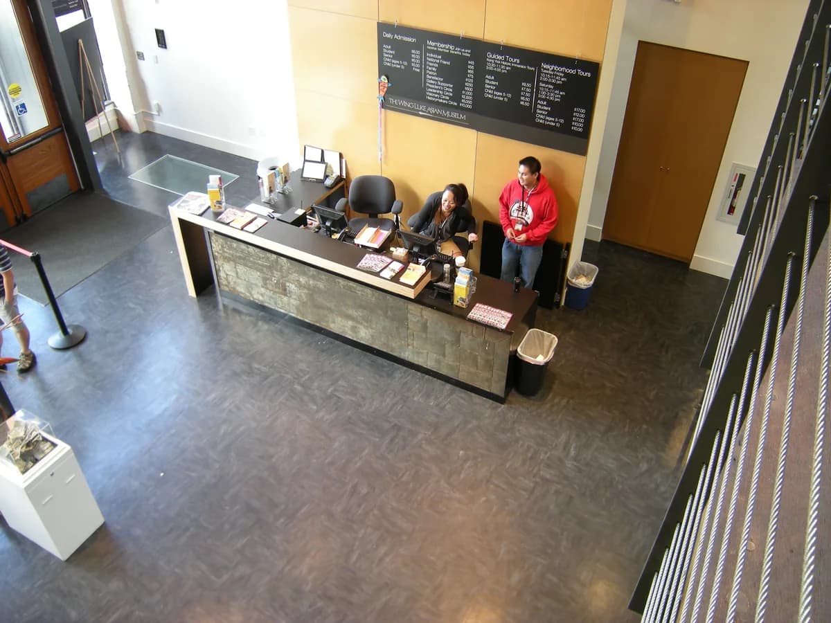The lobby of the Wing Luke Museum, with an admissions desk, a chalkboard sign, polished concrete floors and an old wooden staircase