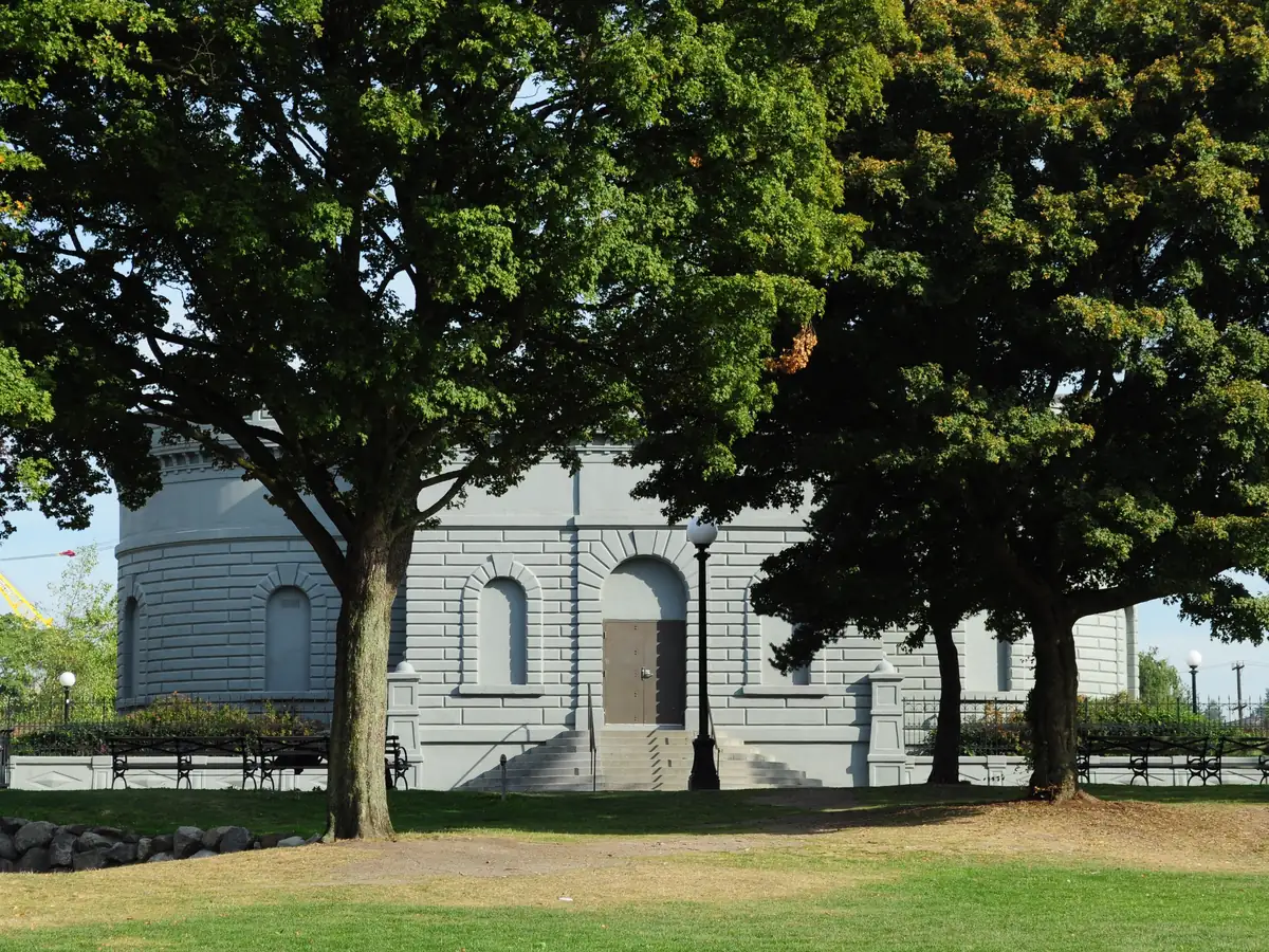 The pale stone gatehouse building at Cal Anderson Park, half hidden behind large shade trees, with a lawn and paths in front