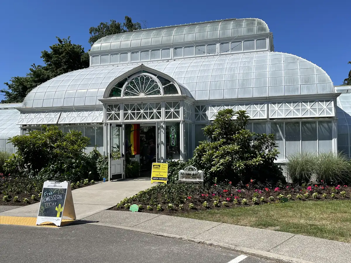 The white Volunteer Park Conservatory, a domed Victorian glasshouse with arched windows, behind flower beds and a path under a blue sky