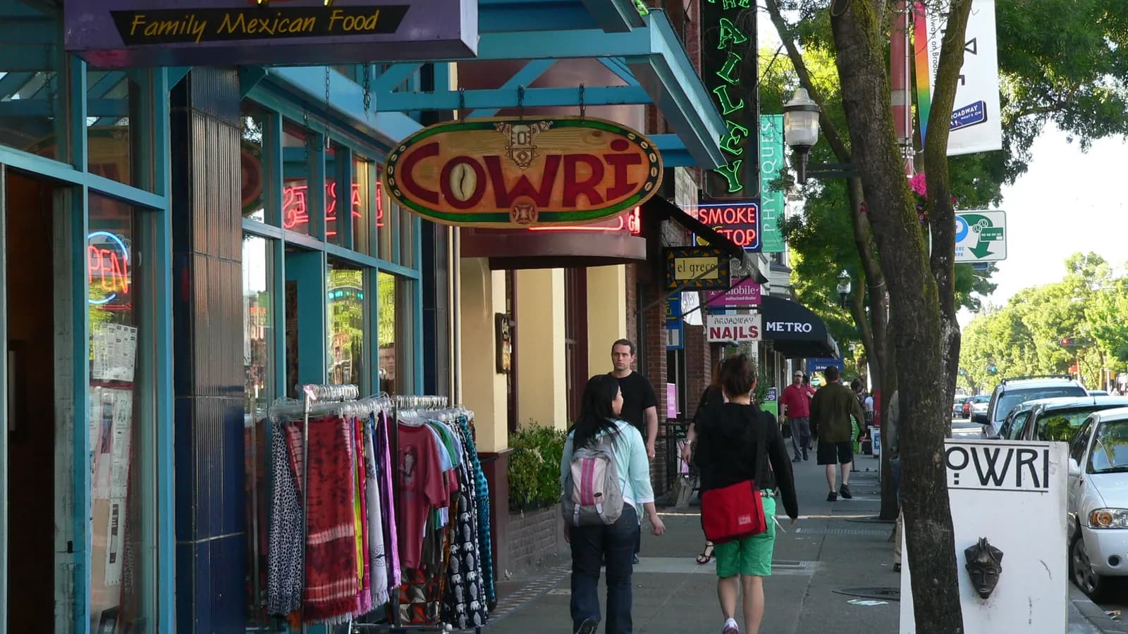 Shops and colorful storefronts along Broadway on Capitol Hill in Seattle, with green street trees and people on the sidewalk