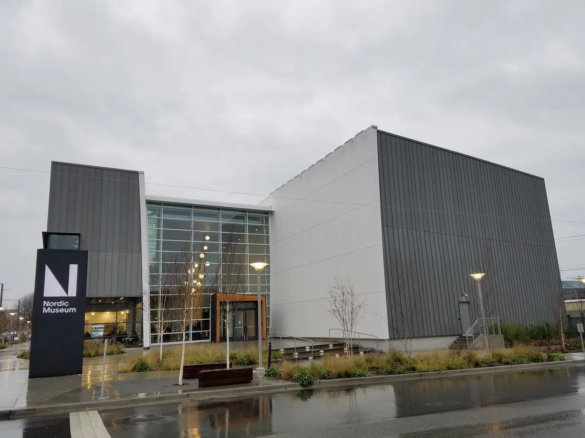 The National Nordic Museum in Ballard, a modern building with tall gray zinc walls and a glass entrance, beside a wet plaza on a cloudy day