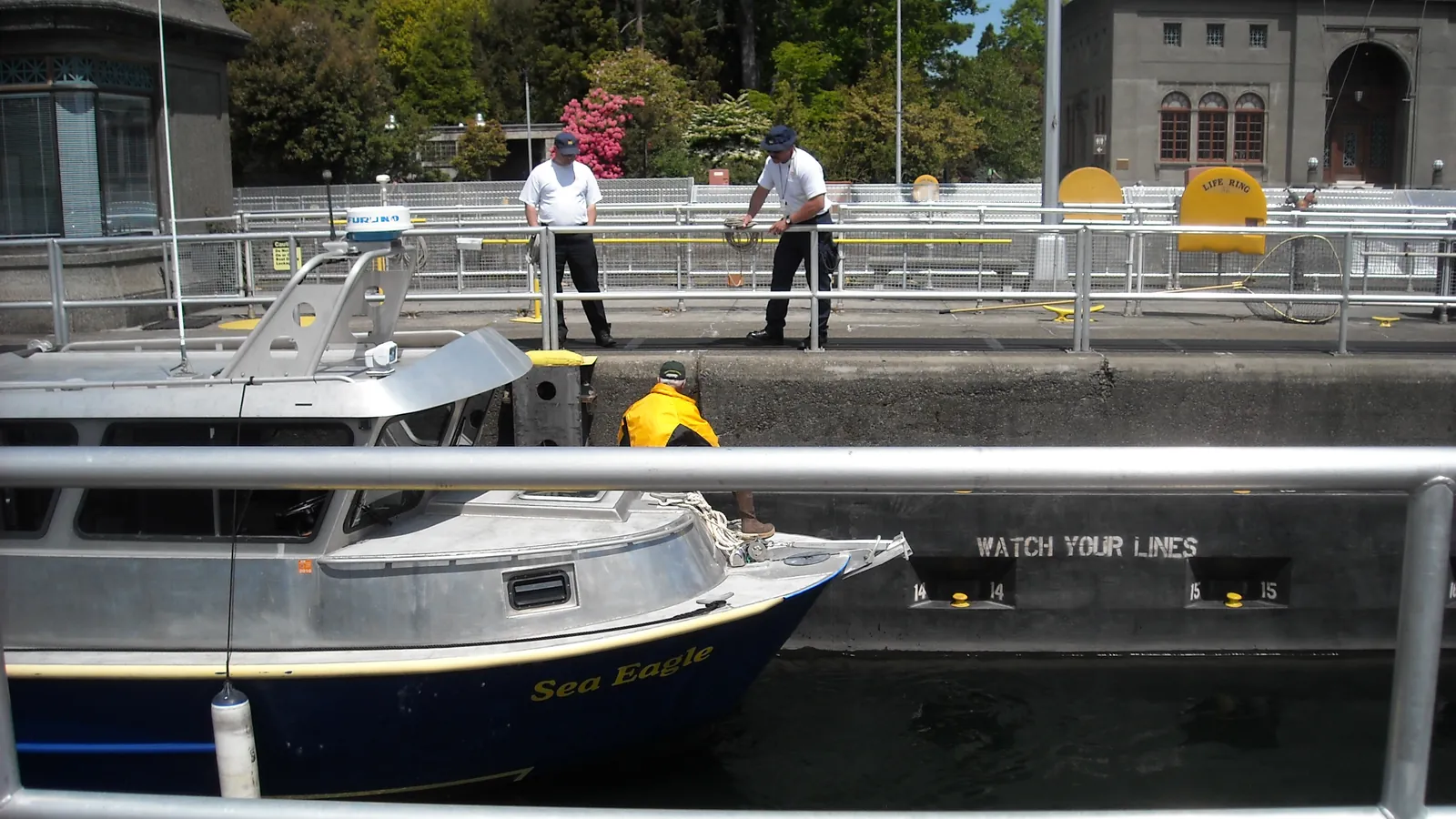 A boat waiting inside the lock chamber at the Ballard Locks in Seattle, with the lock walls, railings and people watching from above