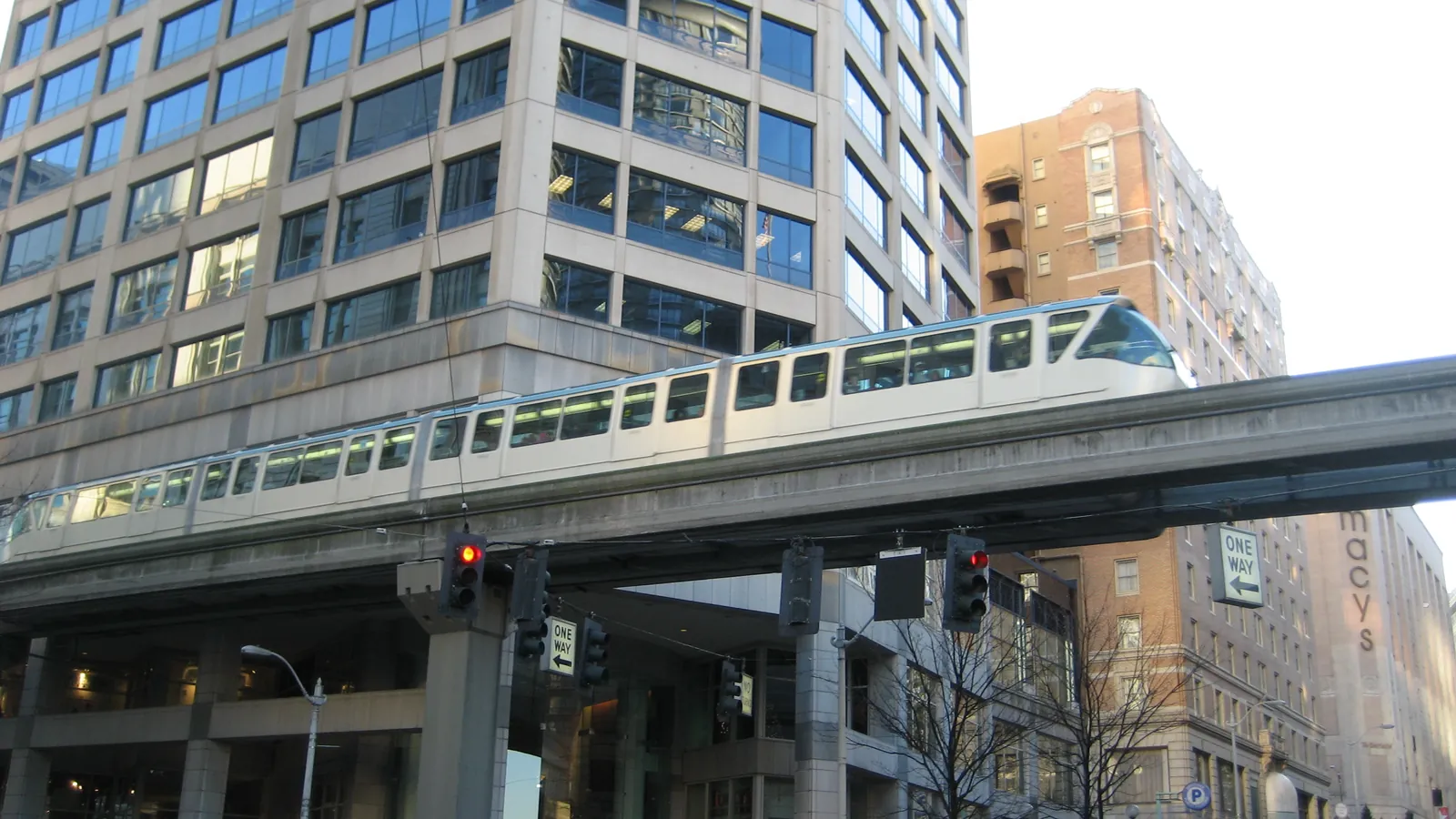 The Seattle Center Monorail train gliding along its elevated concrete track above a downtown street, with buildings on both sides