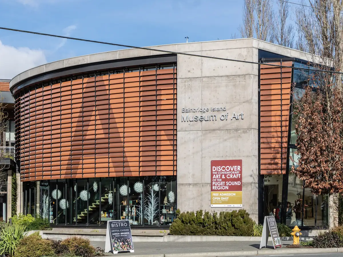 The Bainbridge Island Museum of Art, a modern building with a curved wall of wooden slats and large glass windows, under a blue sky