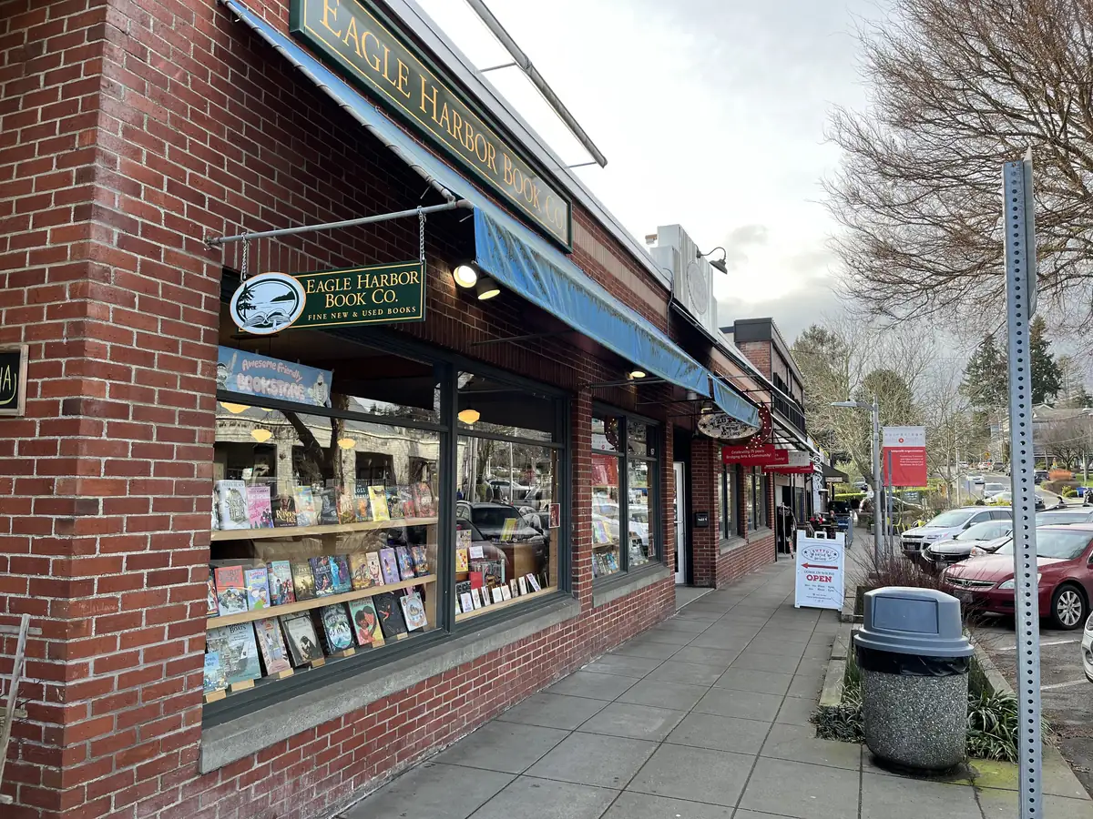 The brick storefront of Eagle Harbor Book Company on Winslow Way, with a blue awning and windows full of books along the sidewalk