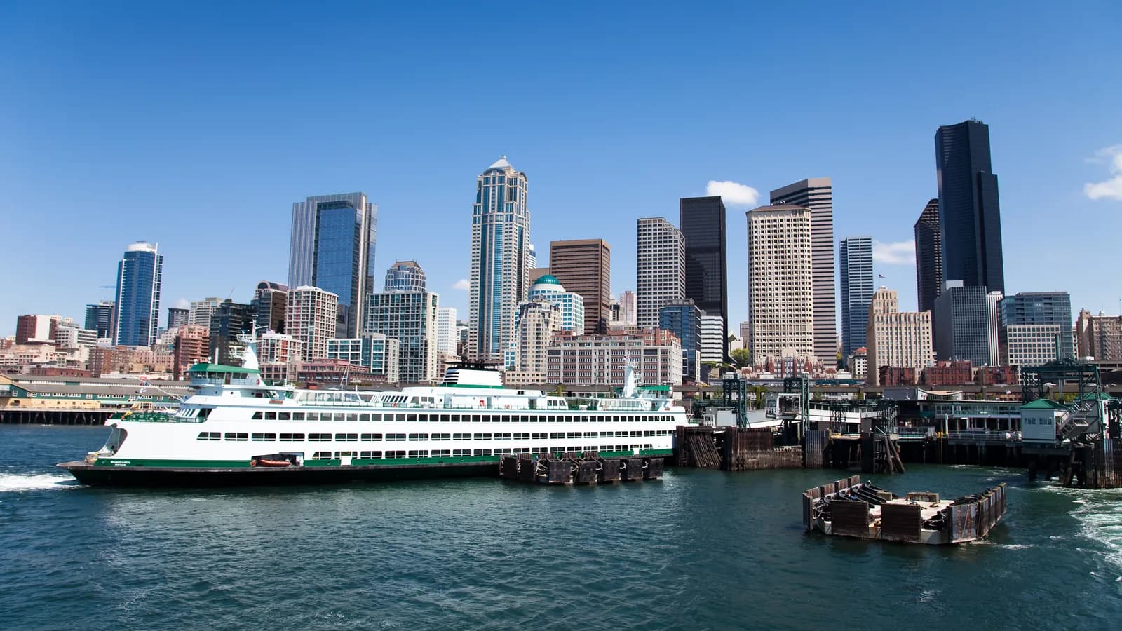 A green and white Washington State ferry crossing Elliott Bay, seen from the water with the downtown Seattle towers behind it