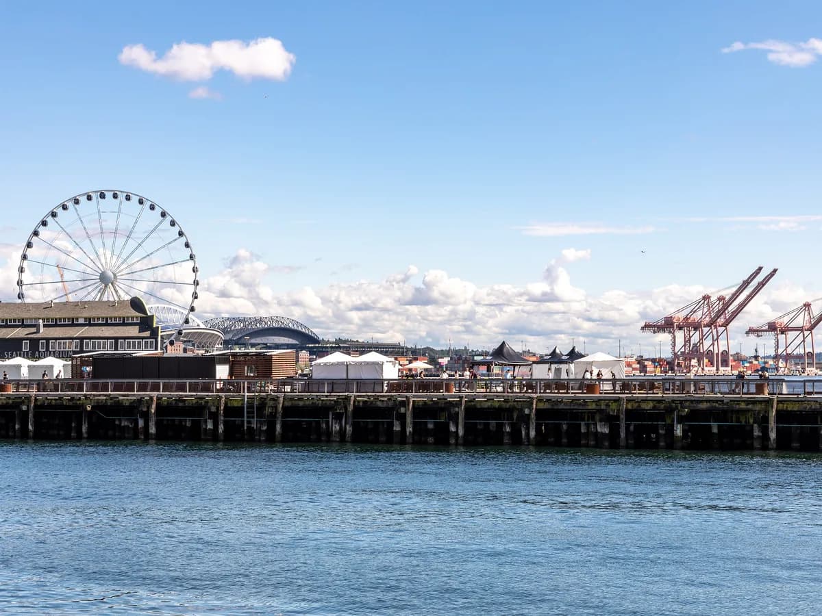 Pier 62 stretches out over the blue water of Elliott Bay, with the Great Wheel at left and container cranes on the far shore